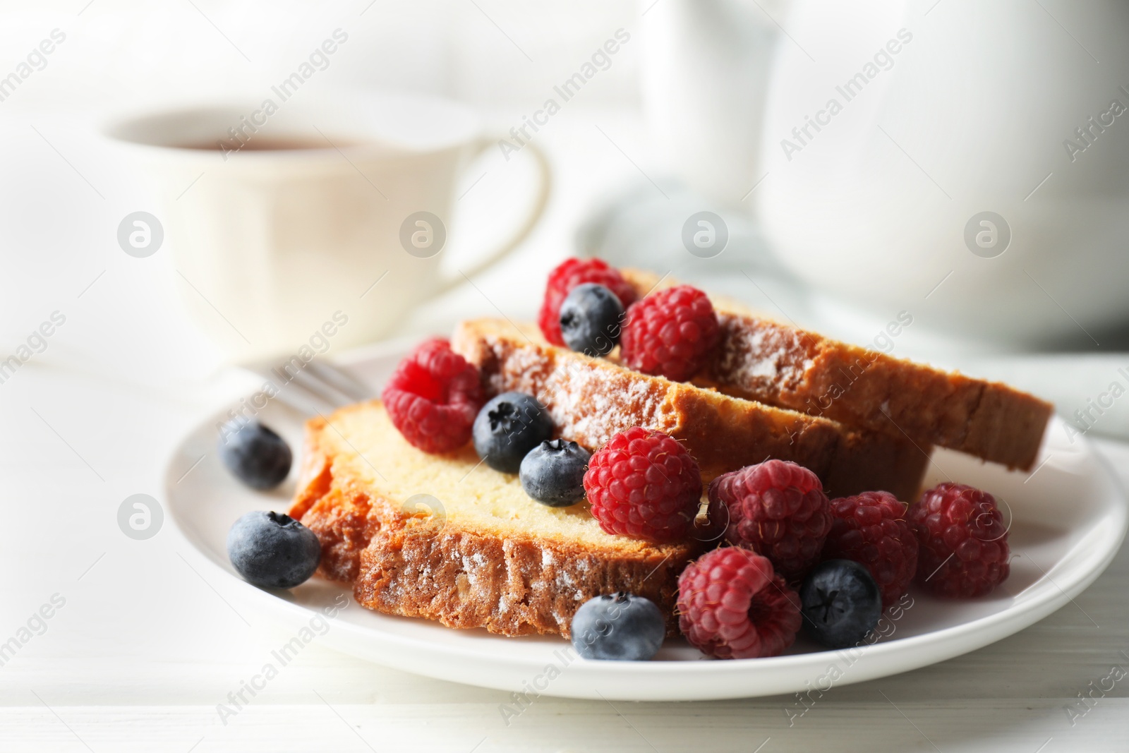 Photo of Freshly baked sponge cake, raspberries and blueberries on white wooden table, closeup