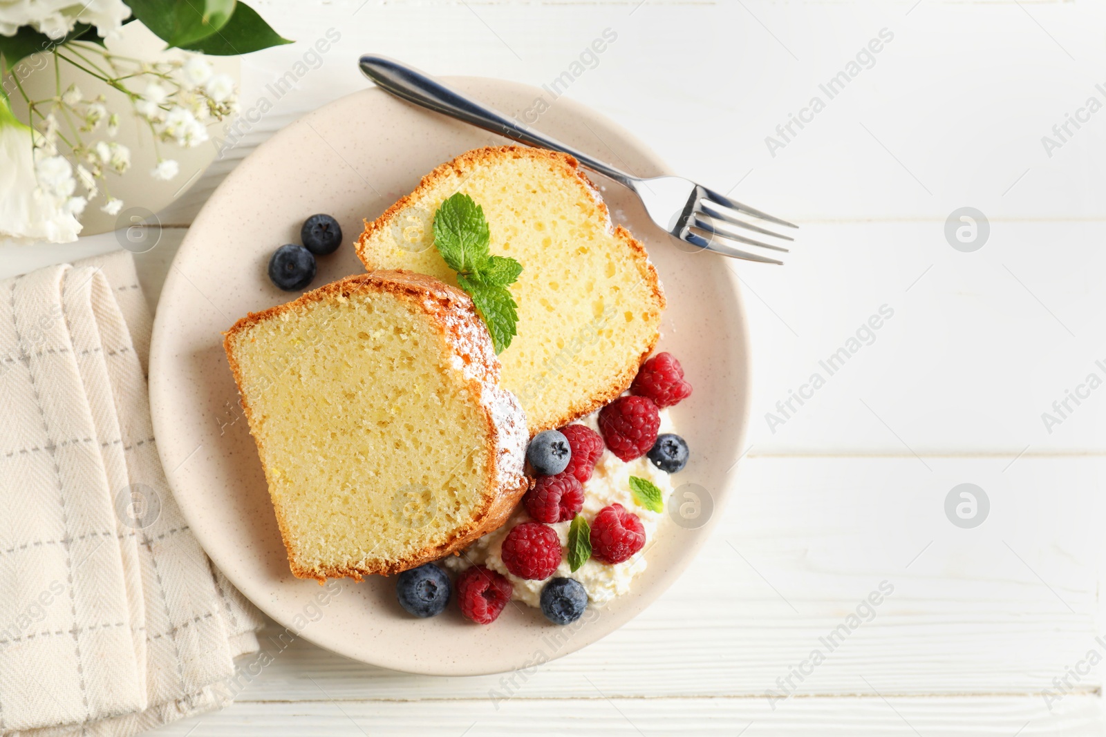 Photo of Freshly baked sponge cake, whipped cream, berries and mint on white wooden table, top view. Space for text