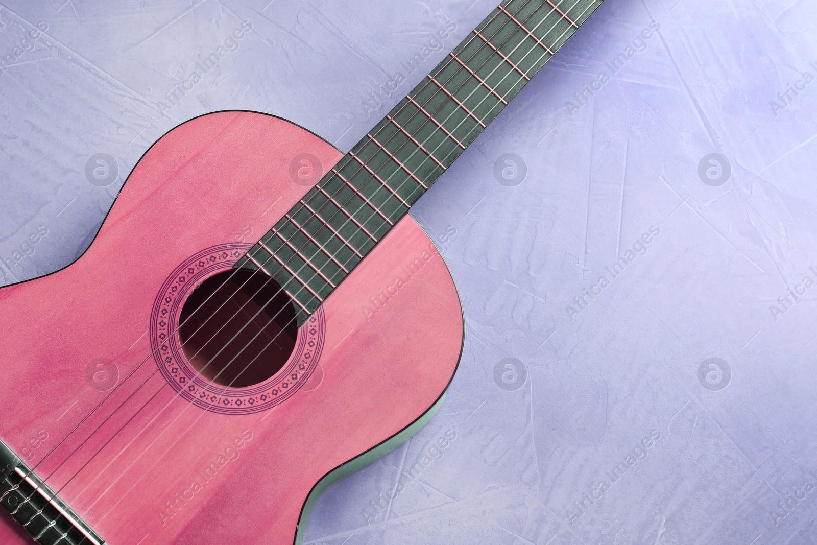 Image of Pink acoustic guitar on violet background, top view. Musical instrument