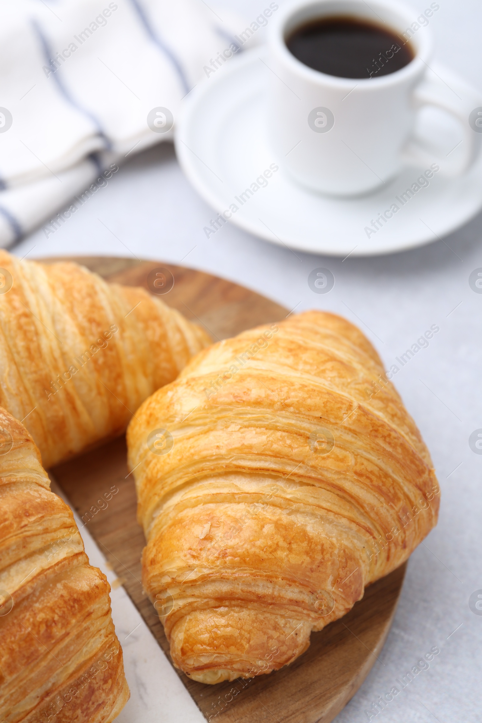 Photo of Tasty fresh croissants and cup of coffee on light table, closeup