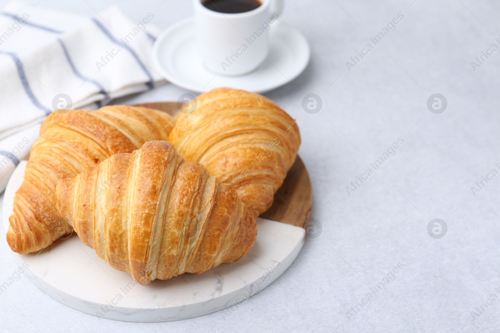 Photo of Tasty fresh croissants and cup of coffee on light table, closeup. Space for text