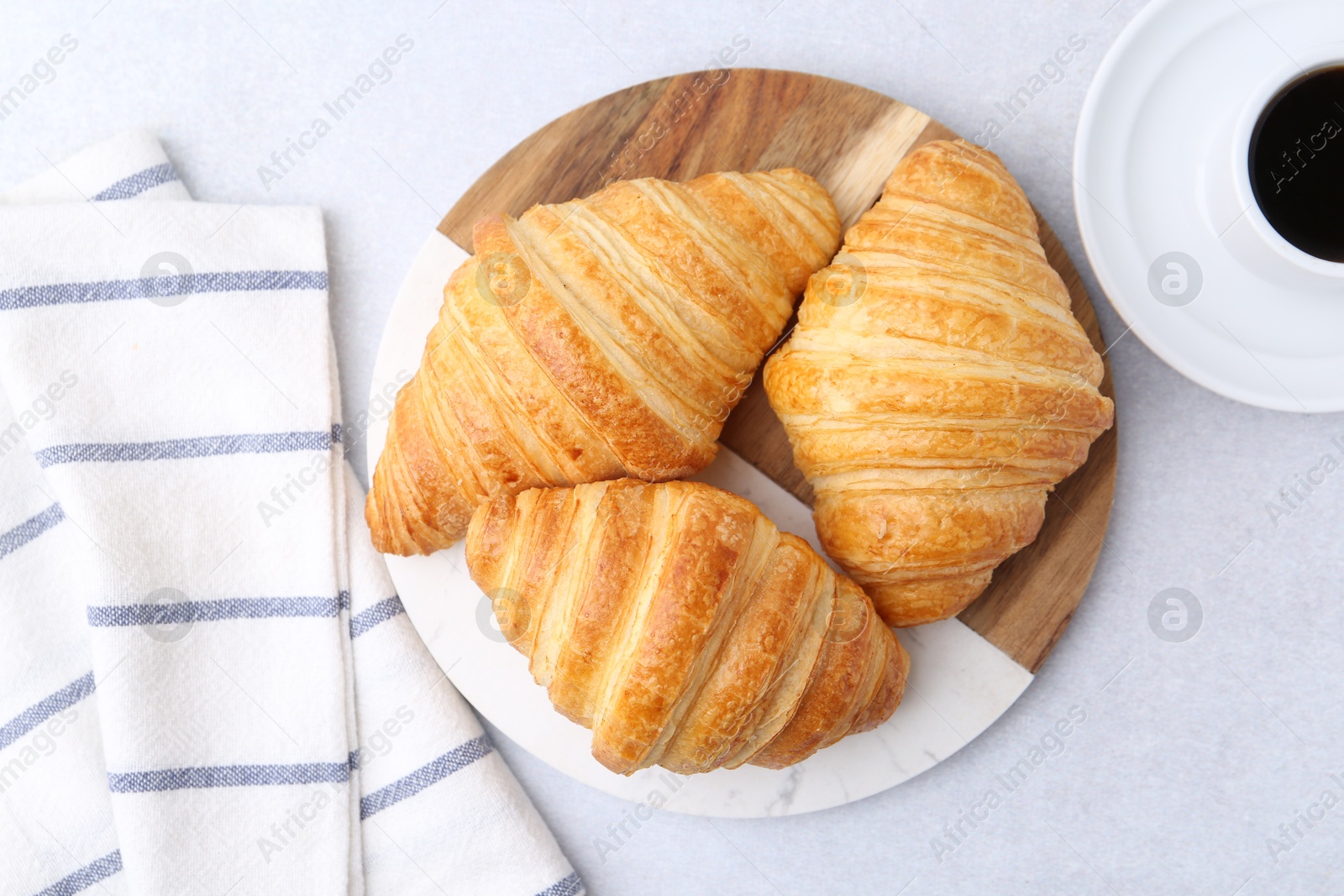 Photo of Tasty fresh croissants and cup of coffee on light grey table, flat lay