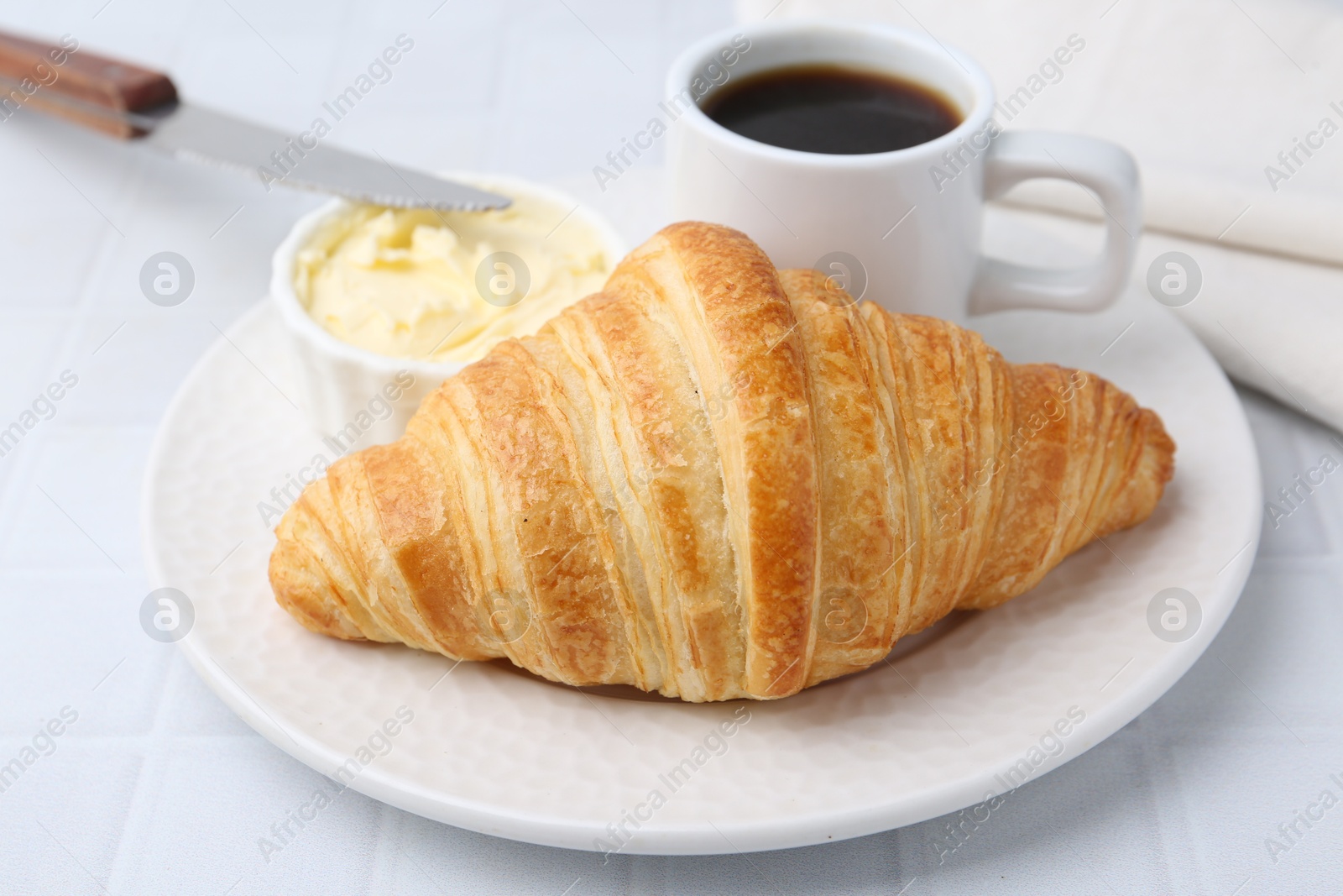 Photo of Tasty fresh croissant served with butter and cup of coffee on white tiled table, closeup