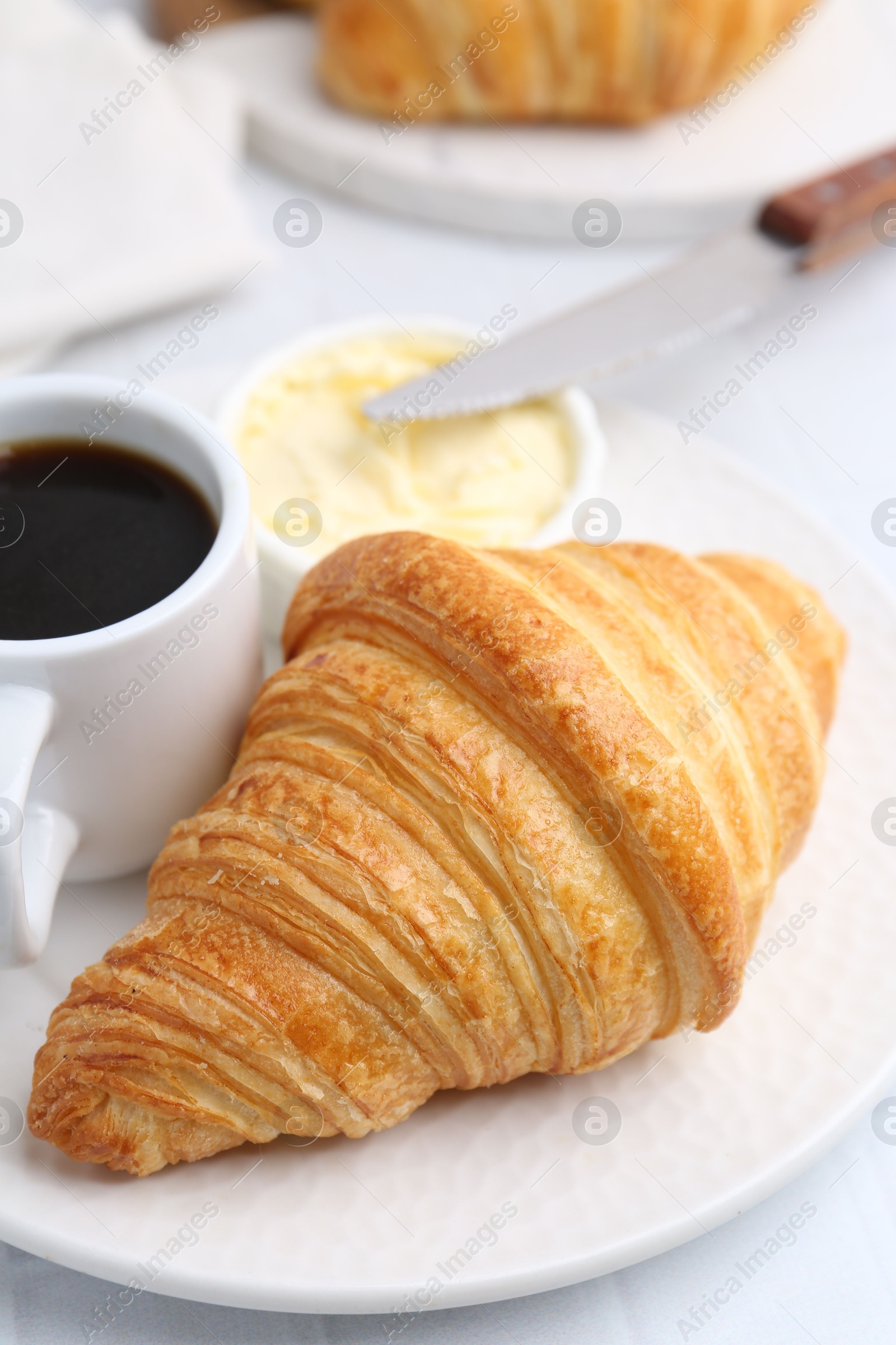 Photo of Tasty fresh croissant served with butter and cup of coffee on white table, closeup