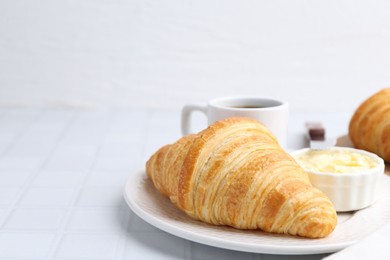 Photo of Tasty fresh croissant served with butter and cup of drink on white tiled table, closeup. Space for text