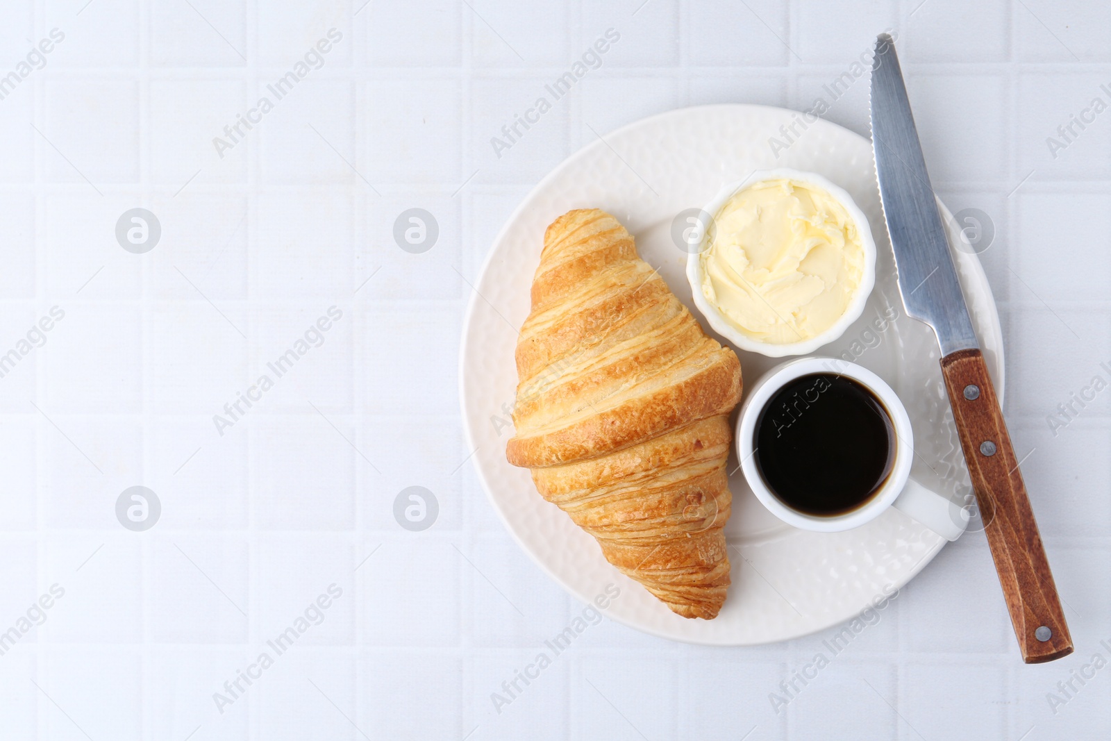 Photo of Tasty fresh croissant served with butter and cup of coffee on white tiled table, top view. Space for text