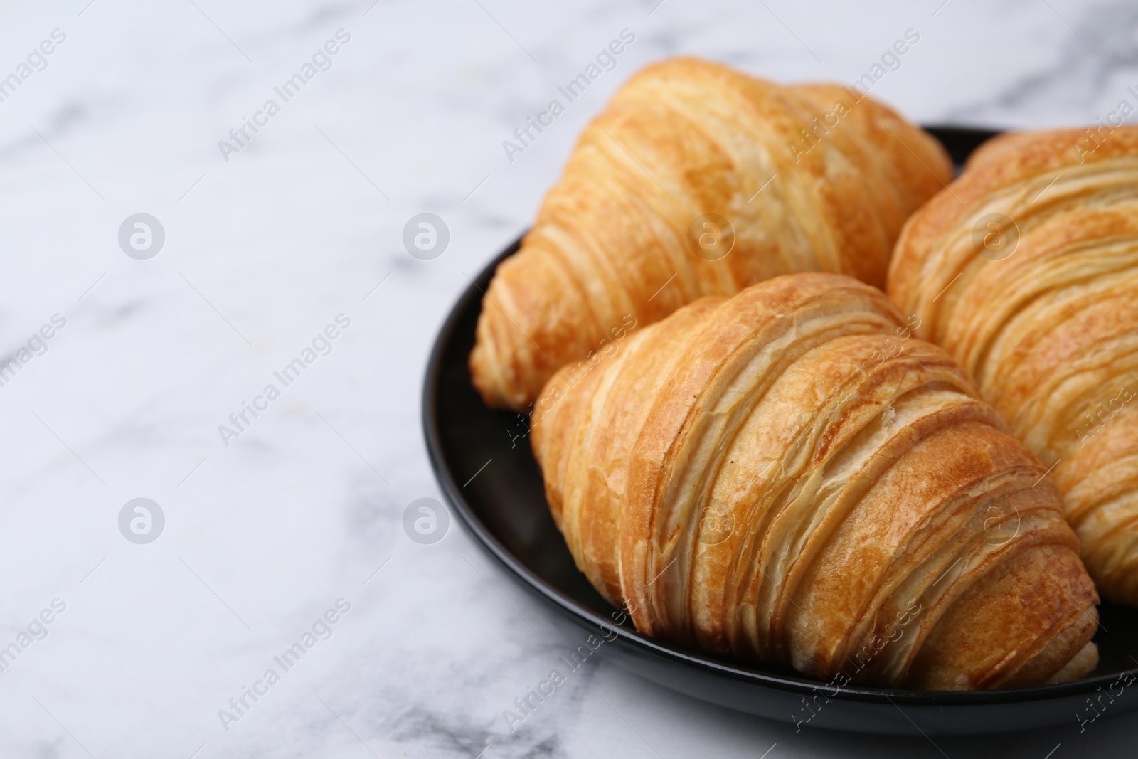 Photo of Tasty fresh croissants on white marble table, closeup. Space for text