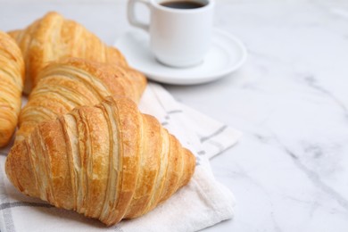 Photo of Tasty fresh croissants and cup of coffee on white marble table, closeup. Space for text