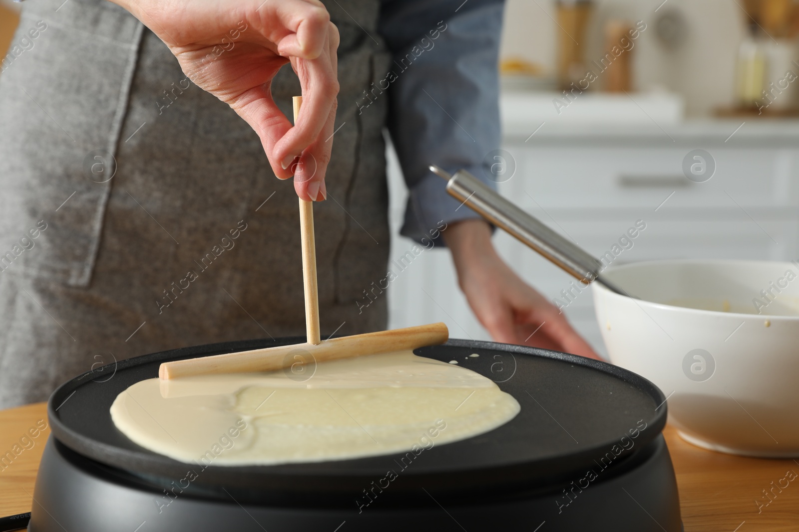 Photo of Woman cooking delicious crepe on electrical pancake maker in kitchen, closeup