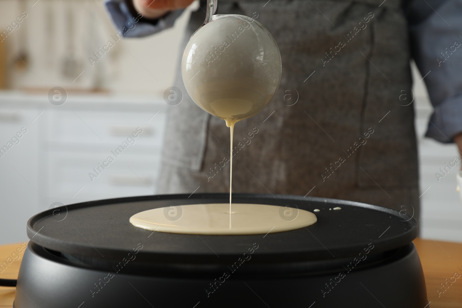 Photo of Woman cooking delicious crepe on electrical pancake maker in kitchen, closeup