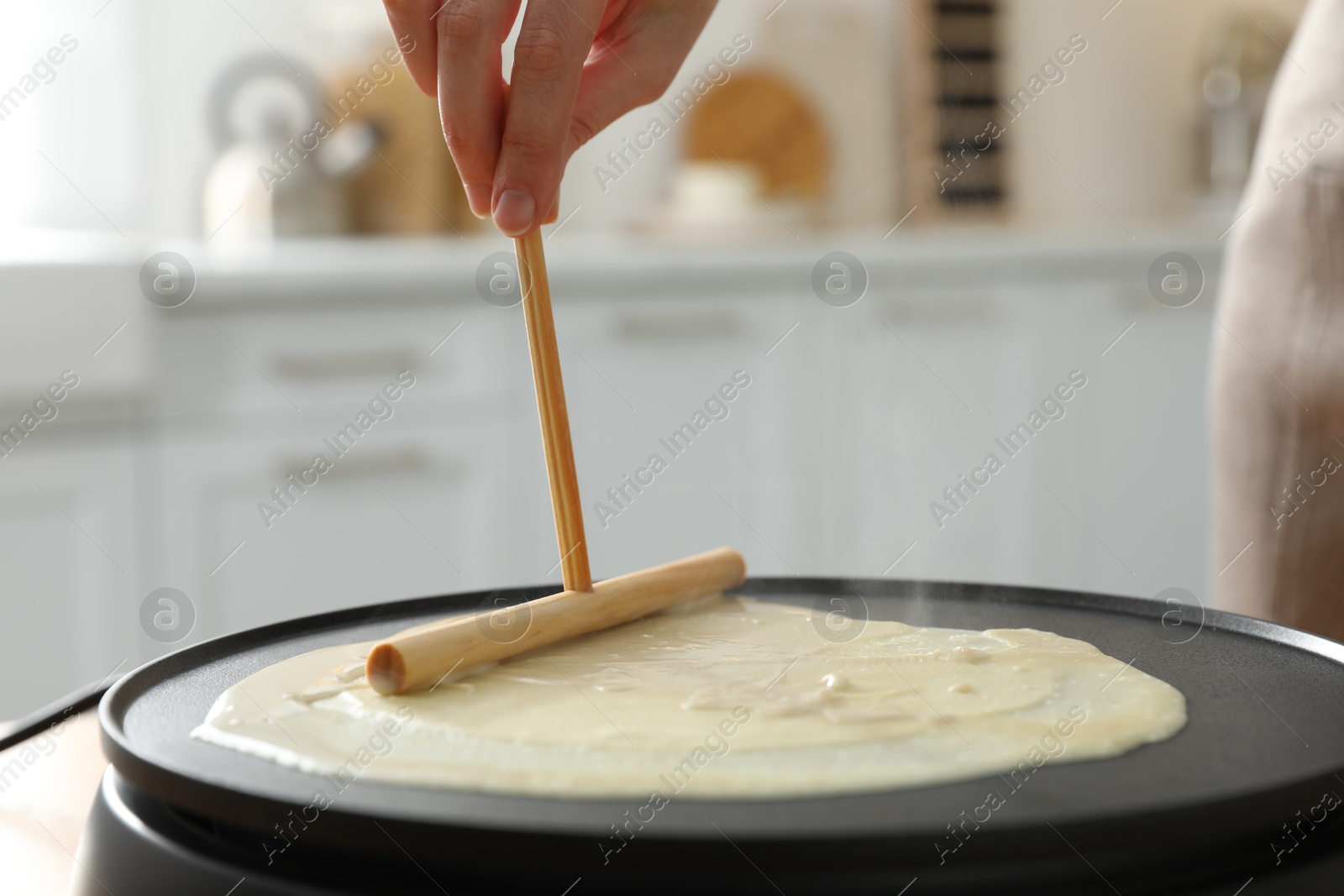 Photo of Woman cooking delicious crepe on electrical pancake maker in kitchen, closeup