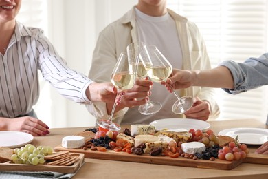 Photo of People clinking glasses of wine at served table, closeup