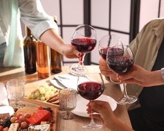 Photo of People clinking glasses of red wine at served table, closeup