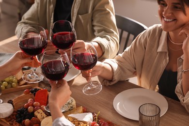 Photo of People clinking glasses of red wine at served table, closeup