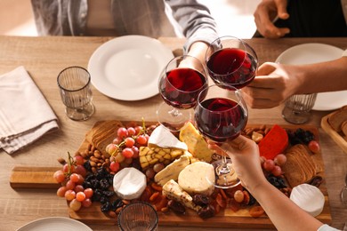 Photo of People clinking glasses of red wine at served table, closeup