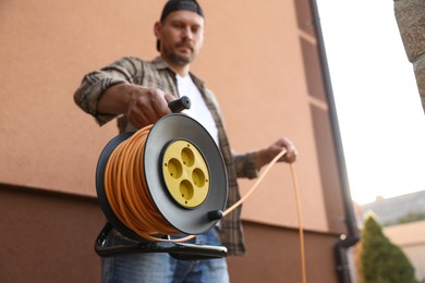 Photo of Man with extension cord reel outdoors, selective focus