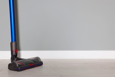 Photo of One cordless vacuum cleaner near grey wall indoors. Space for text