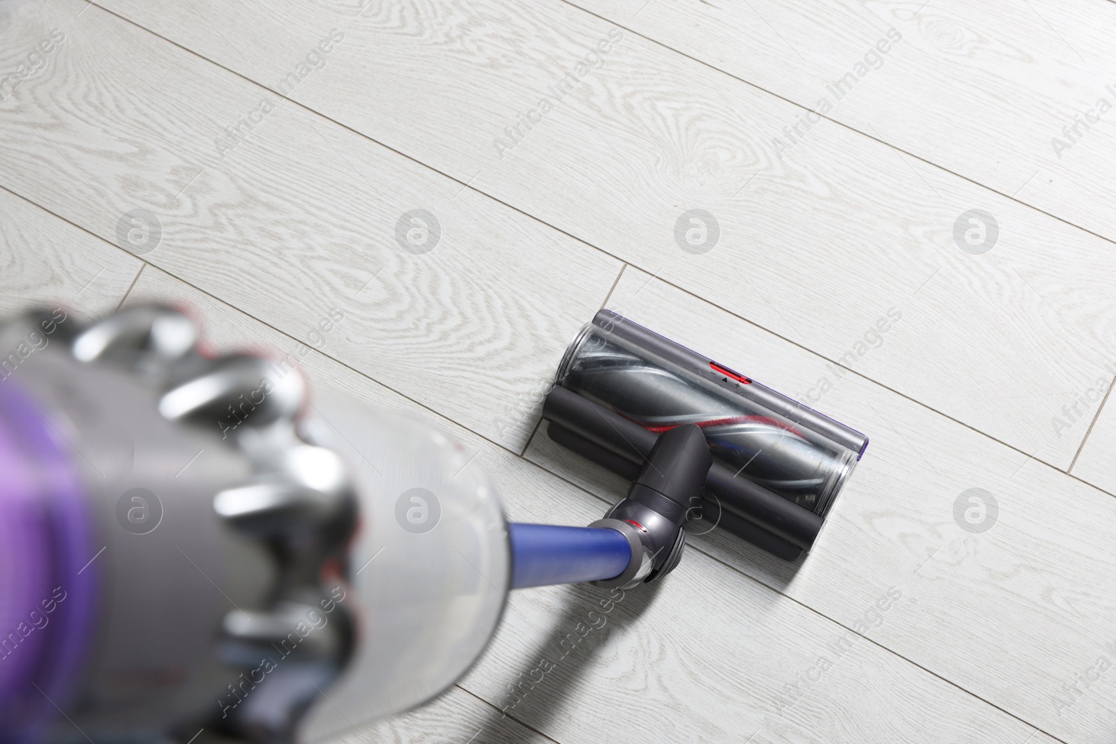 Photo of Cleaning floor with cordless vacuum cleaner indoors, closeup