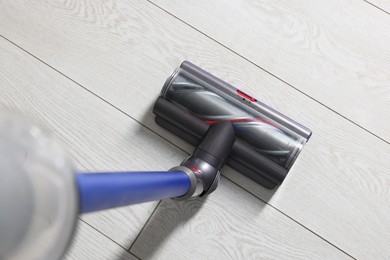 Photo of Cleaning floor with cordless vacuum cleaner indoors, closeup