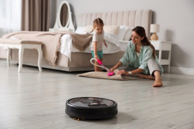 Photo of Mother spending time with her daughter in bedroom, focus on robotic vacuum cleaner