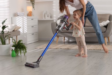 Photo of Young woman and her daughter cleaning floor with cordless vacuum cleaner at home, closeup