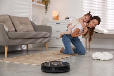 Photo of Mother spending time with her daughter in room, focus on robotic vacuum cleaner