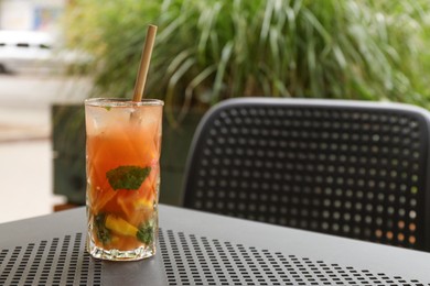 Photo of Glass of tasty refreshing drink and straw on table in outdoor cafe