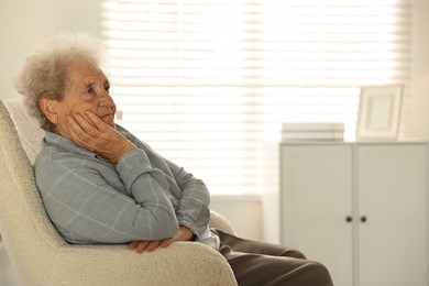 Photo of Loneliness concept. Sad senior woman sitting in armchair at home