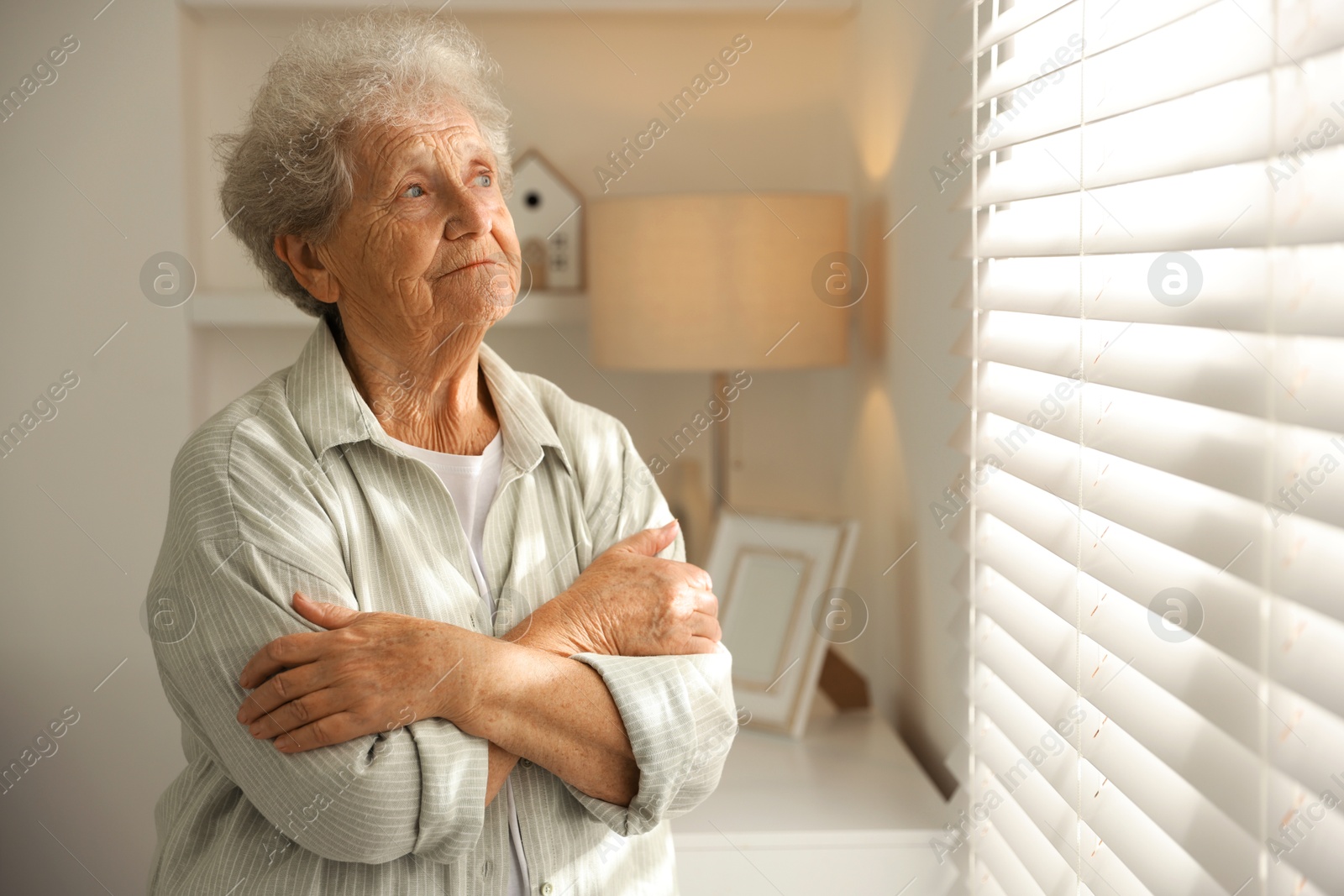 Photo of Loneliness concept. Sad senior woman near window at home