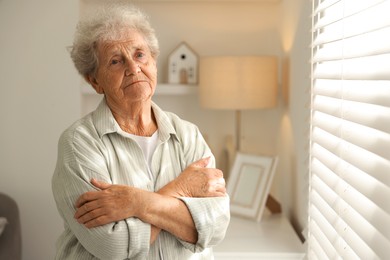 Photo of Loneliness concept. Sad senior woman near window at home