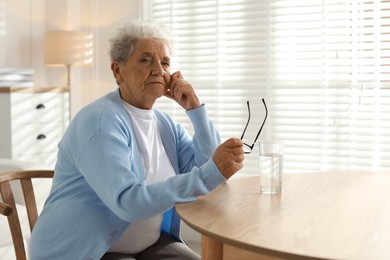 Photo of Sad senior woman feeling lonely at table with glass of water indoors