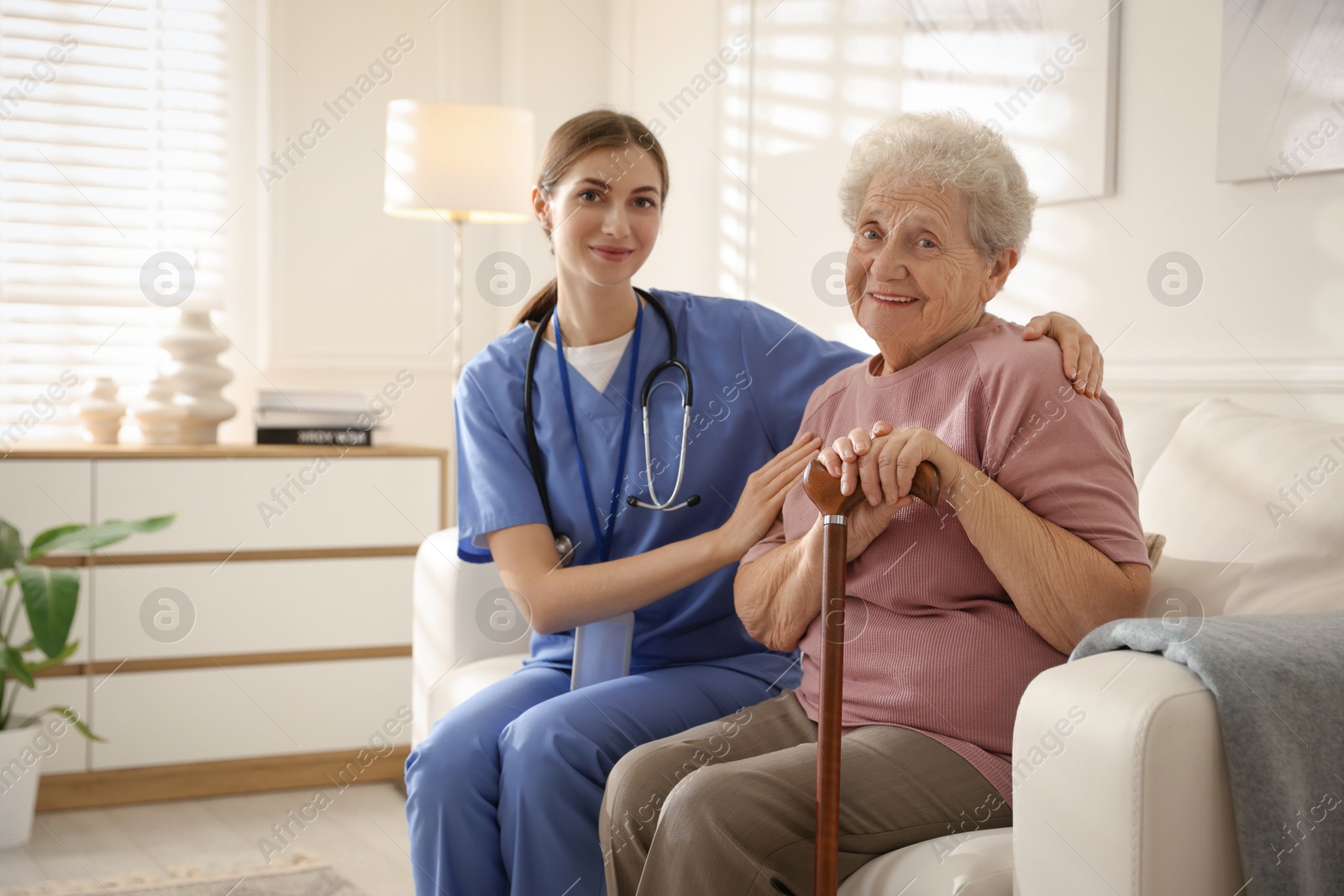 Photo of Caregiver supporting senior woman on sofa. Home health care service