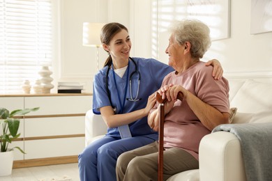 Photo of Caregiver supporting senior woman on sofa. Home health care service