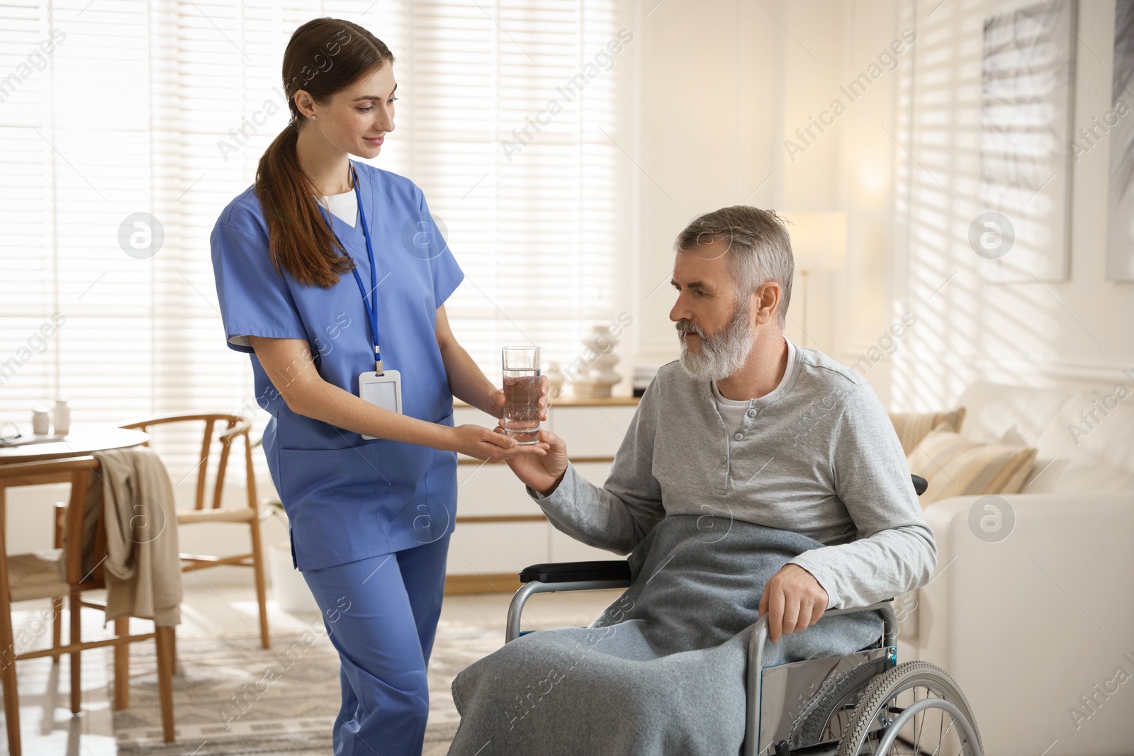 Photo of Caregiver giving glass of water to senior man indoors. Home health care service