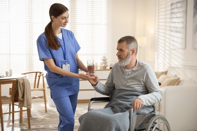 Photo of Caregiver giving glass of water to senior man indoors. Home health care service