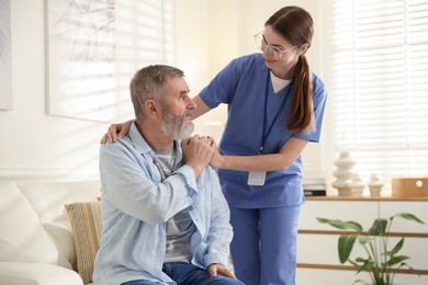 Photo of Caregiver supporting senior man indoors. Home health care service