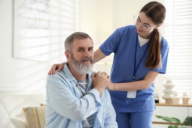 Photo of Caregiver supporting senior man indoors. Home health care service