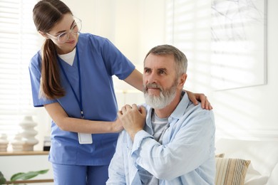 Photo of Caregiver supporting senior man indoors. Home health care service