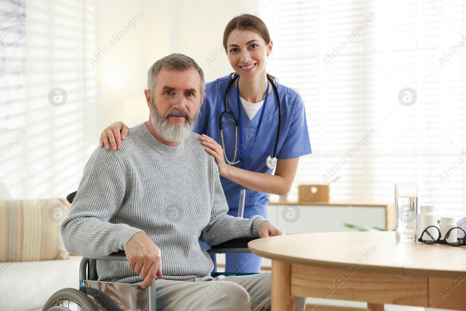 Photo of Caregiver assisting senior man in wheelchair indoors. Home health care service