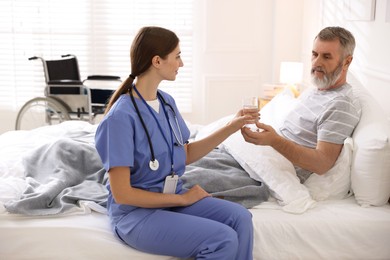 Photo of Caregiver giving water to senior man on bed indoors. Home health care service