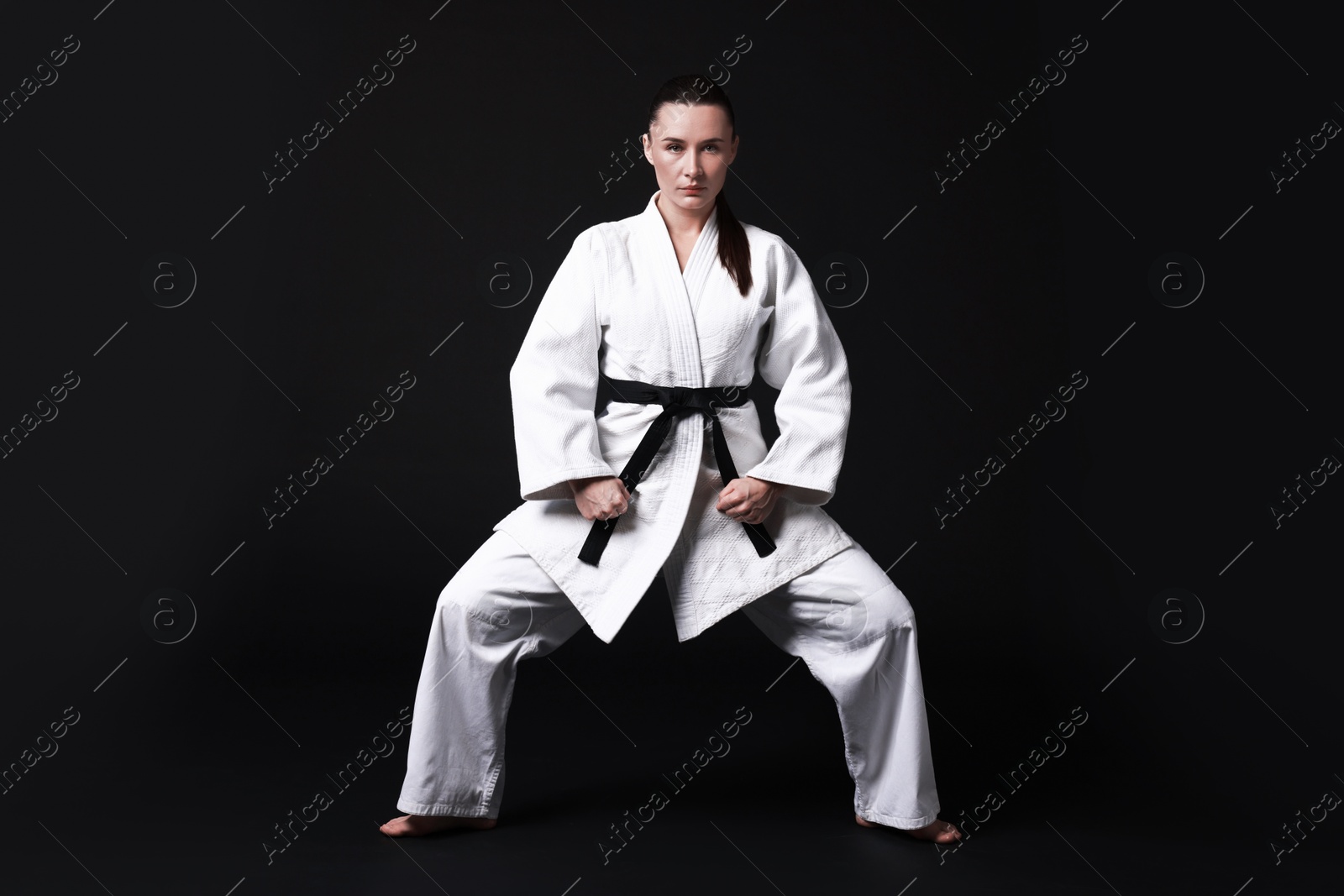 Photo of Young woman in kimono practicing karate on black background