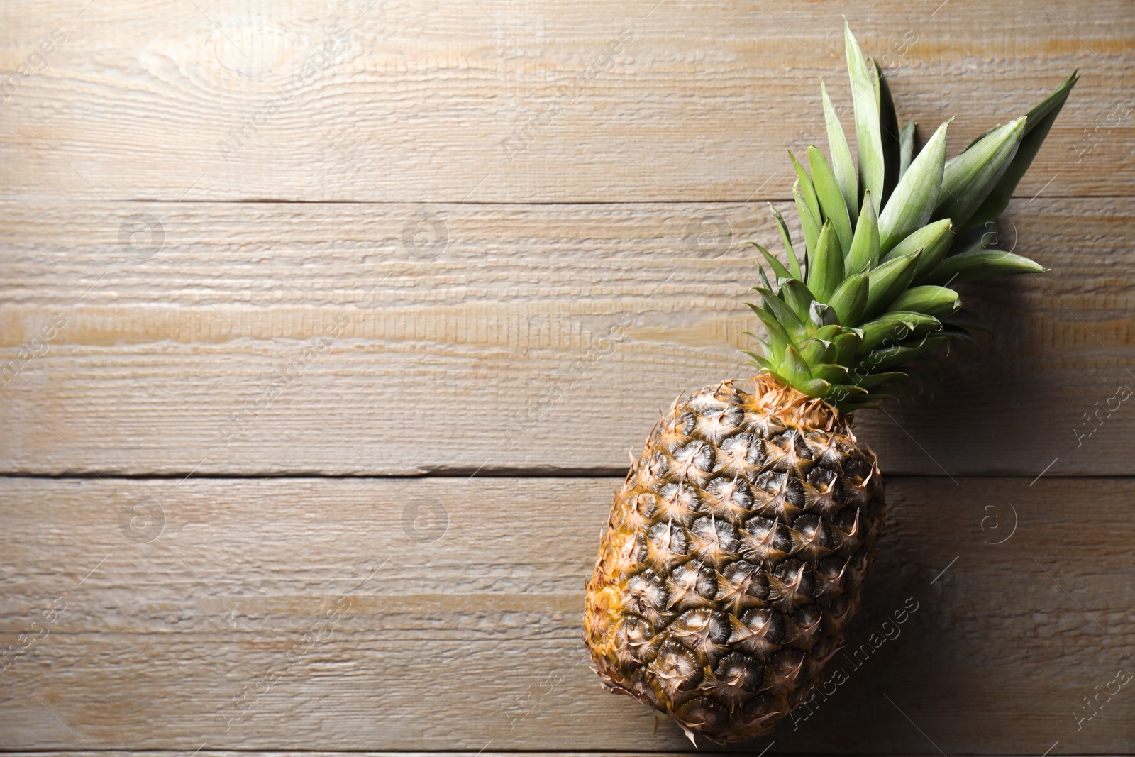 Photo of Fresh ripe pineapple on wooden table, top view. Space for text