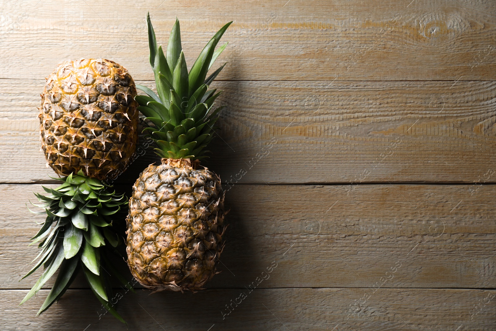 Photo of Fresh ripe pineapples on wooden table, flat lay. Space for text