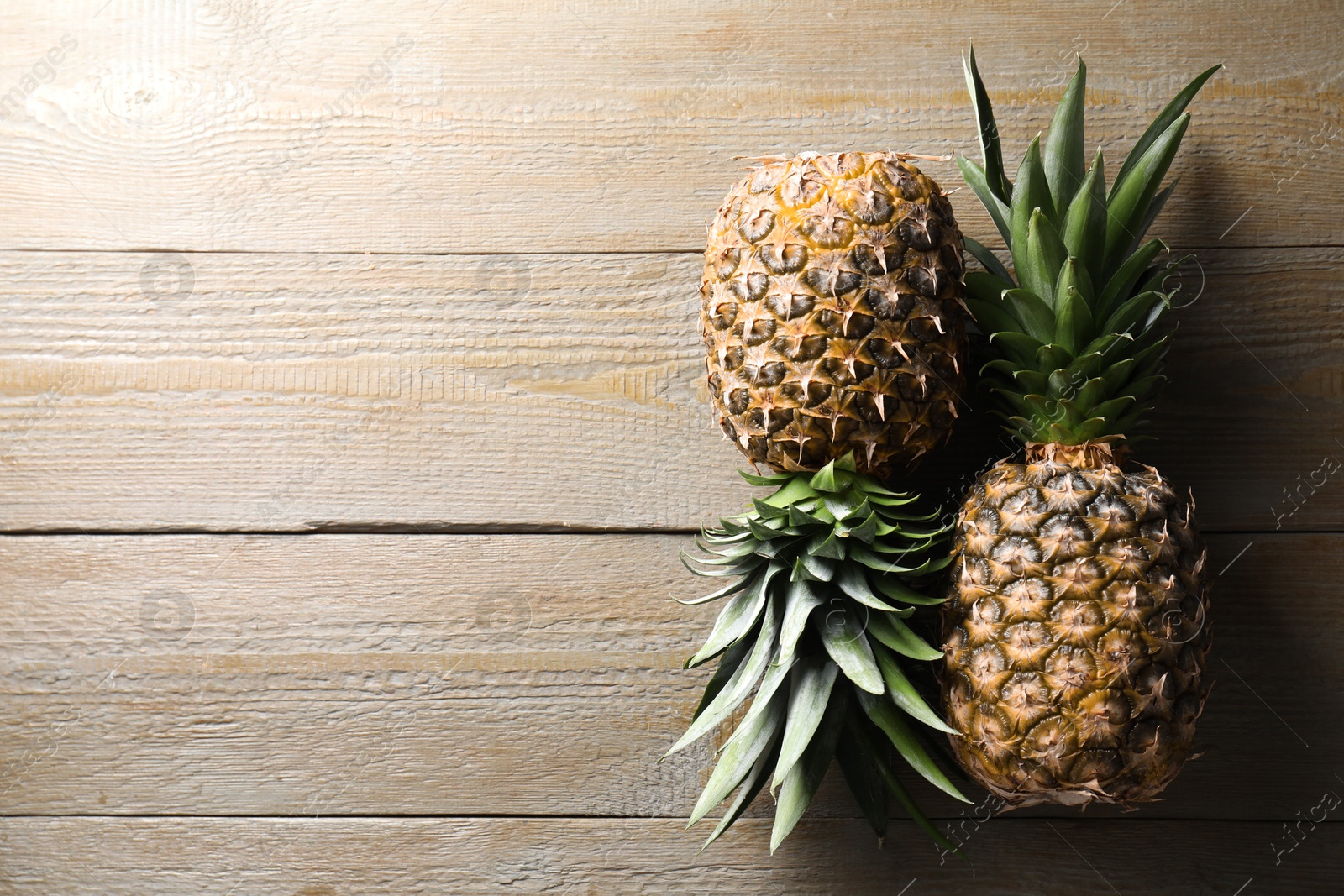 Photo of Fresh ripe pineapples on wooden table, flat lay. Space for text