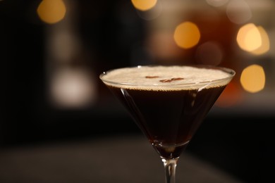 Photo of Delicious espresso martini in glass against blurred lights, closeup