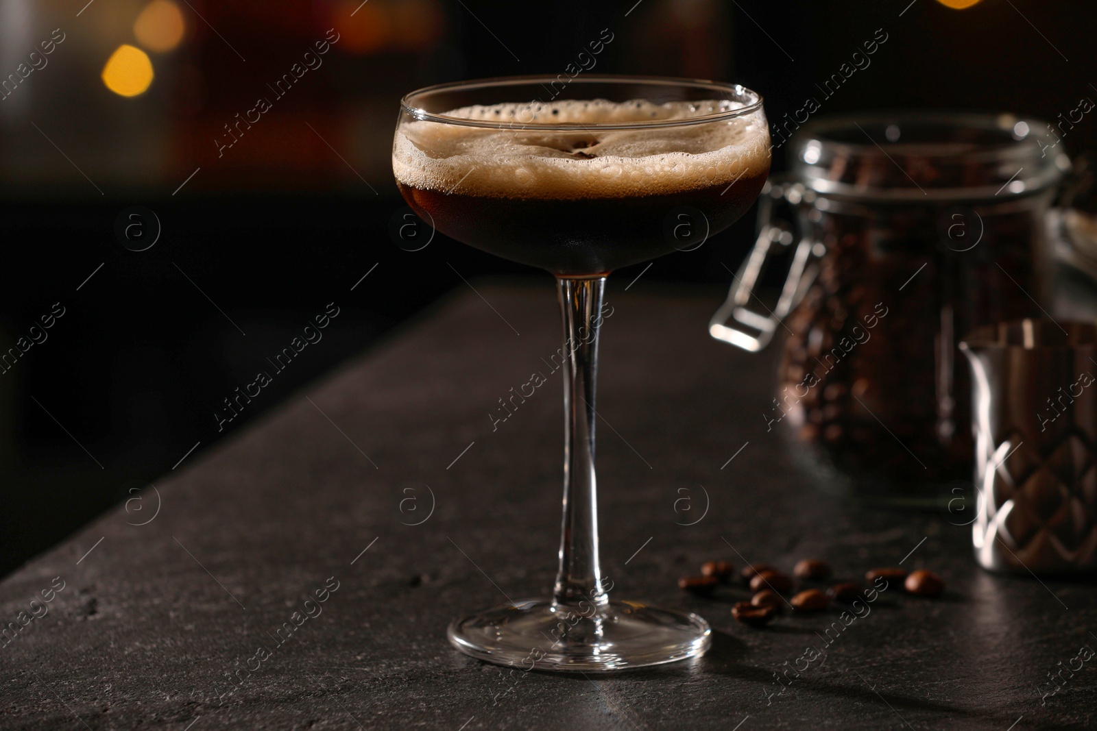 Photo of Glass with delicious espresso martini and coffee beans on dark table in bar, closeup. Space for text