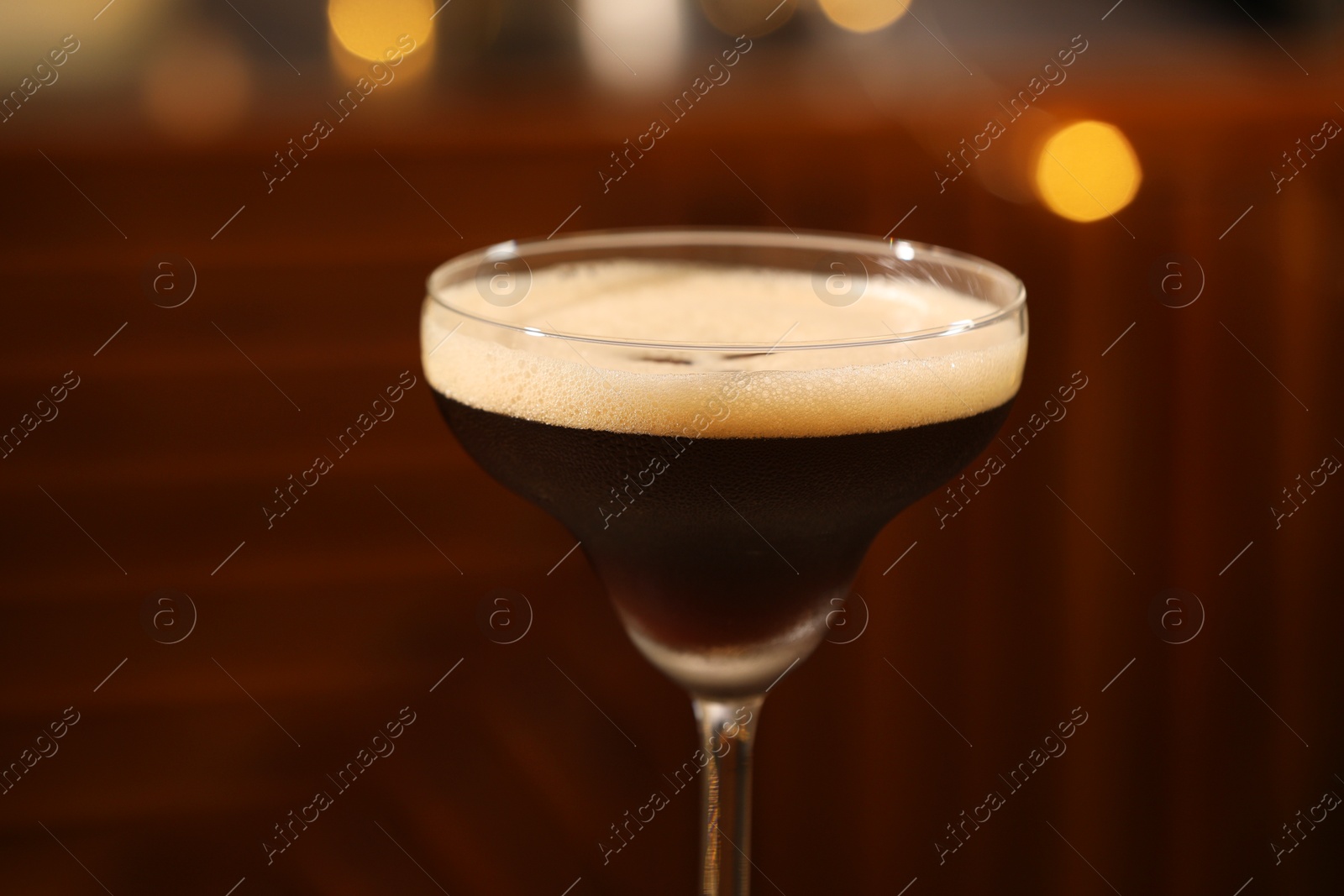 Photo of Delicious espresso martini in glass against blurred lights, closeup