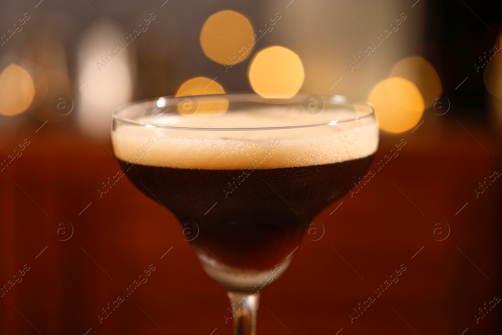 Photo of Delicious espresso martini in glass against blurred lights, closeup