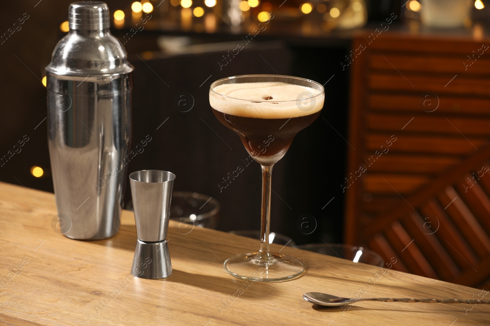 Photo of Glass with delicious espresso martini, jigger and shaker on wooden table in bar