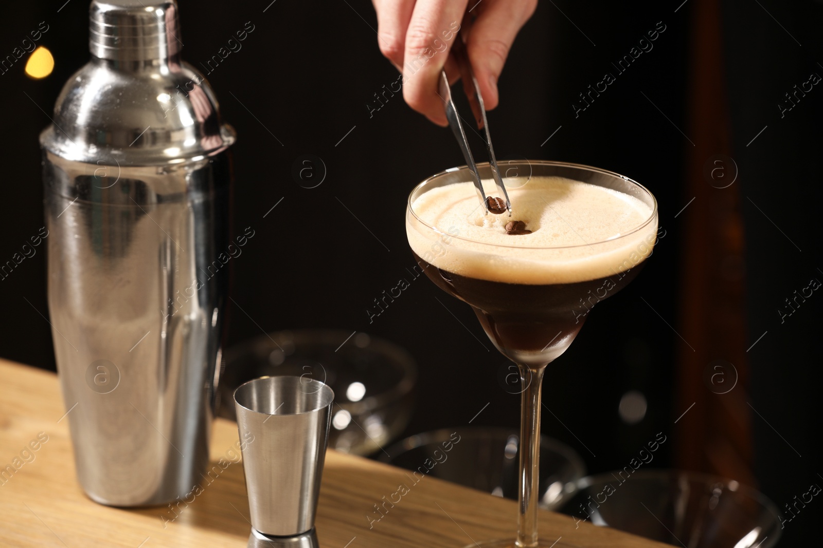 Photo of Bartender putting coffee bean into glass with delicious espresso martini at wooden table in bar, closeup